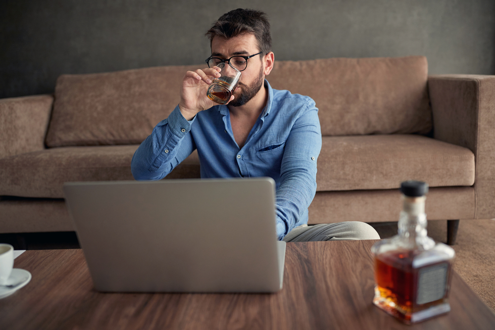 young man drinking whiskey while looking at the laptop screen